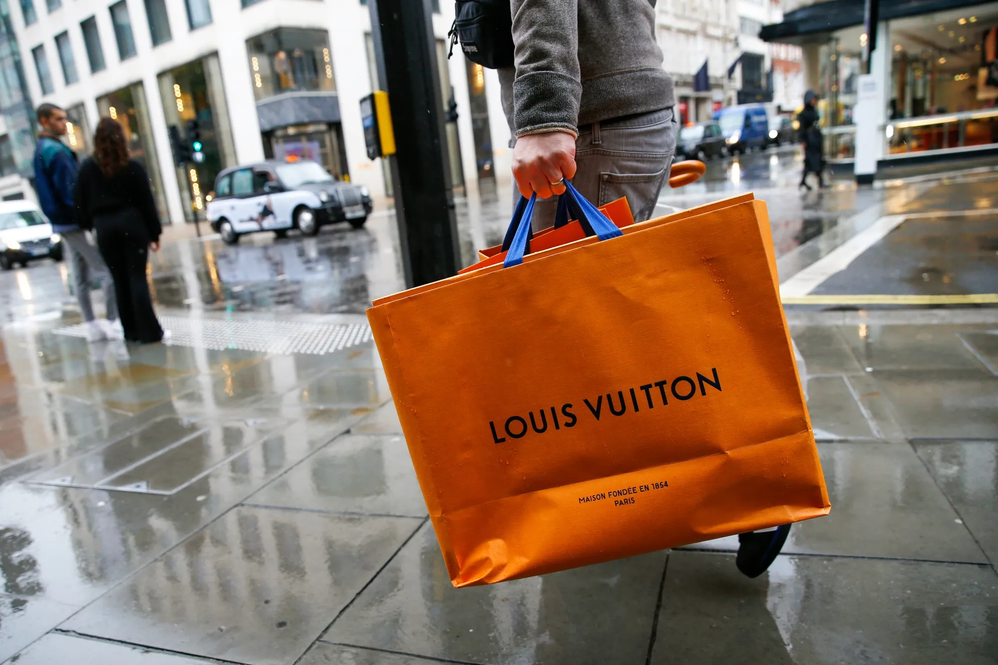A pedestrian carries a Louis Vuitton shopping bag.