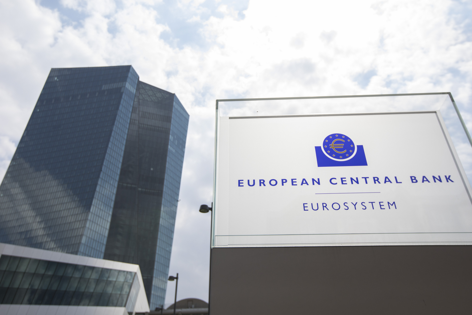 A euro currency symbol sits on a eurosystem sign outside the the European Central Bank (ECB) headquarters in Frankfurt, Germany, on Thursday, April 27, 2017. The ECB kept interest rates unchanged at record lows and maintained its quantitative-easing program as officials monitor the economic recovery and the risk of political turbulence in the region.