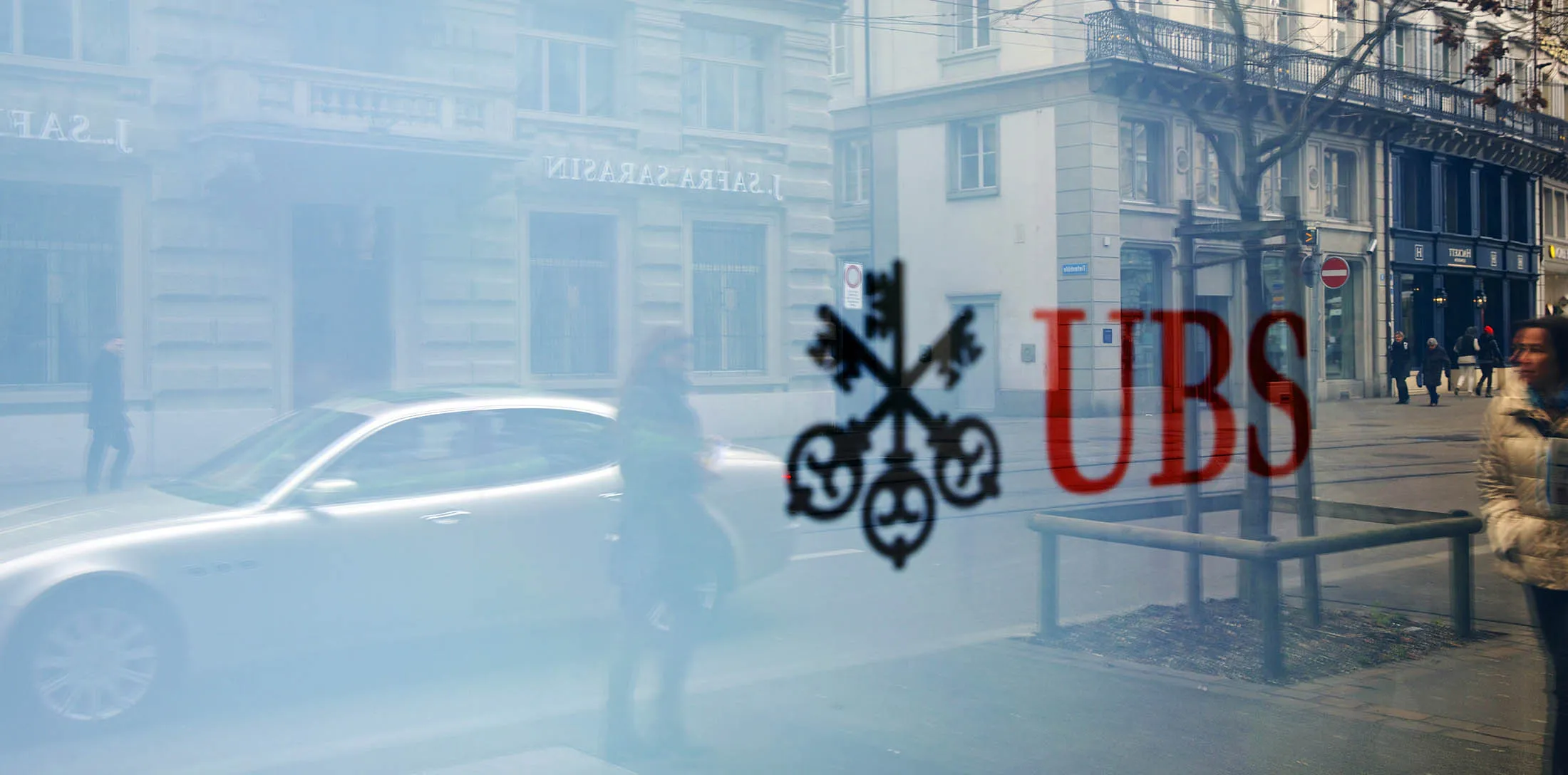 Pedestrians are reflected in the window of a UBS bank branch in Zurich.
