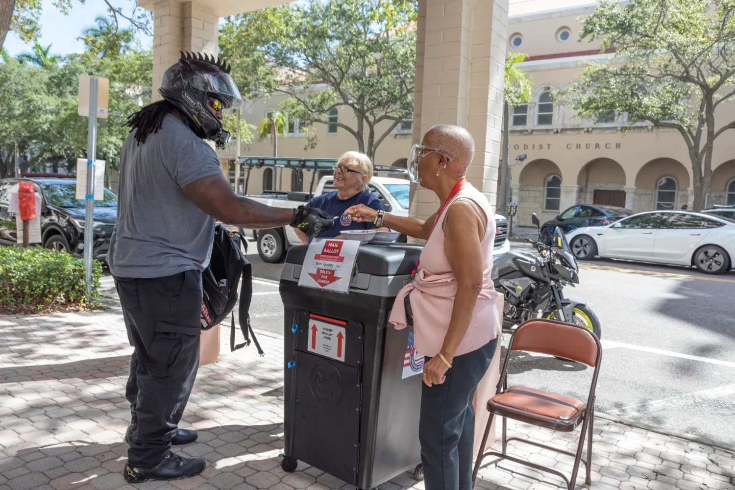 An election official hands an "I Voted" sticker to a voter dropping off a mail-in ballot outside of a polling location in Saint Petersburg, Florida, in 2022.