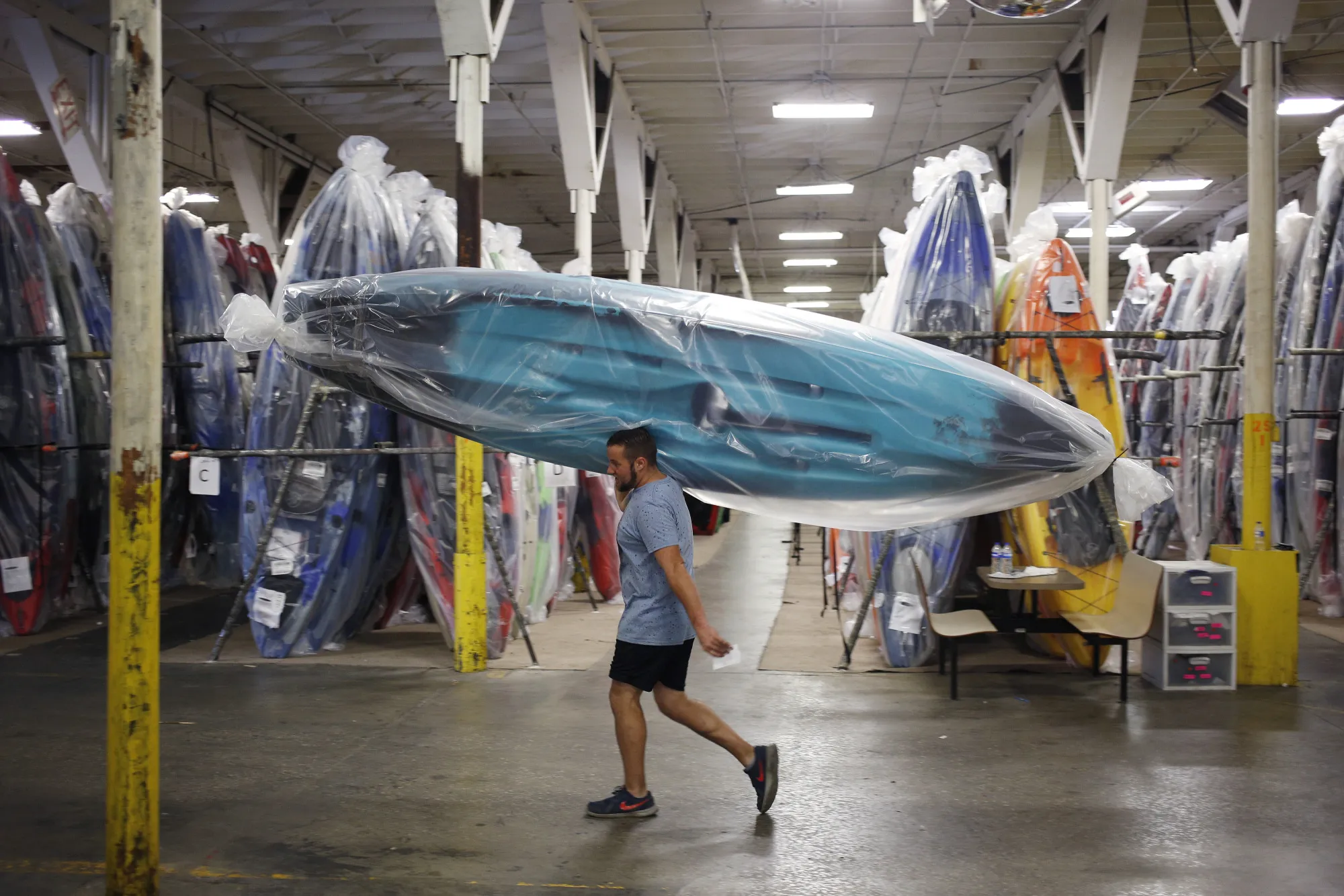 An employee carries a newly manufactured plastic kayak towards the loading dock at the Jackson Kayak Inc. factory in Sparta, Tennessee.