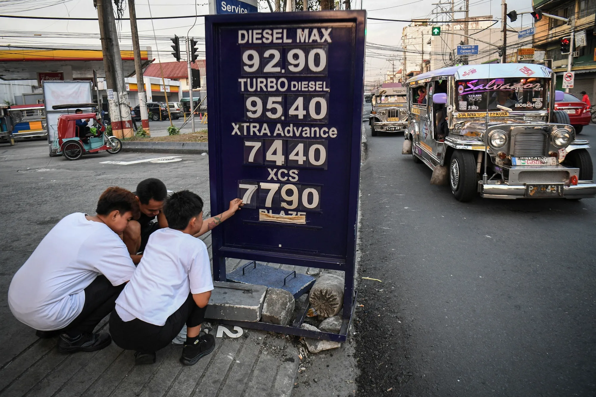 Workers change the price label of fuel at a petrol station in Manila on March 17.