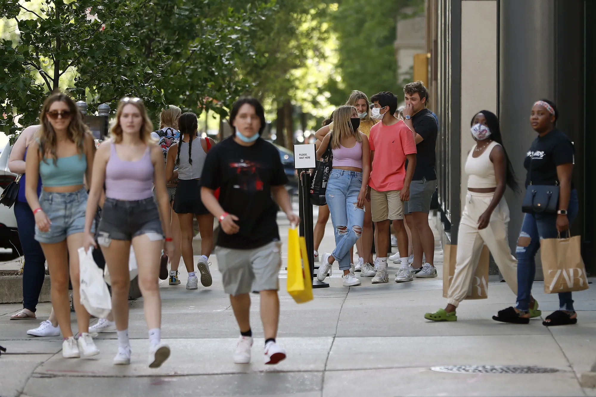 Shoppers wait in line outside of a Chicago downtown retail store as pedestrians pass by, Wednesday, May 26, 2021.