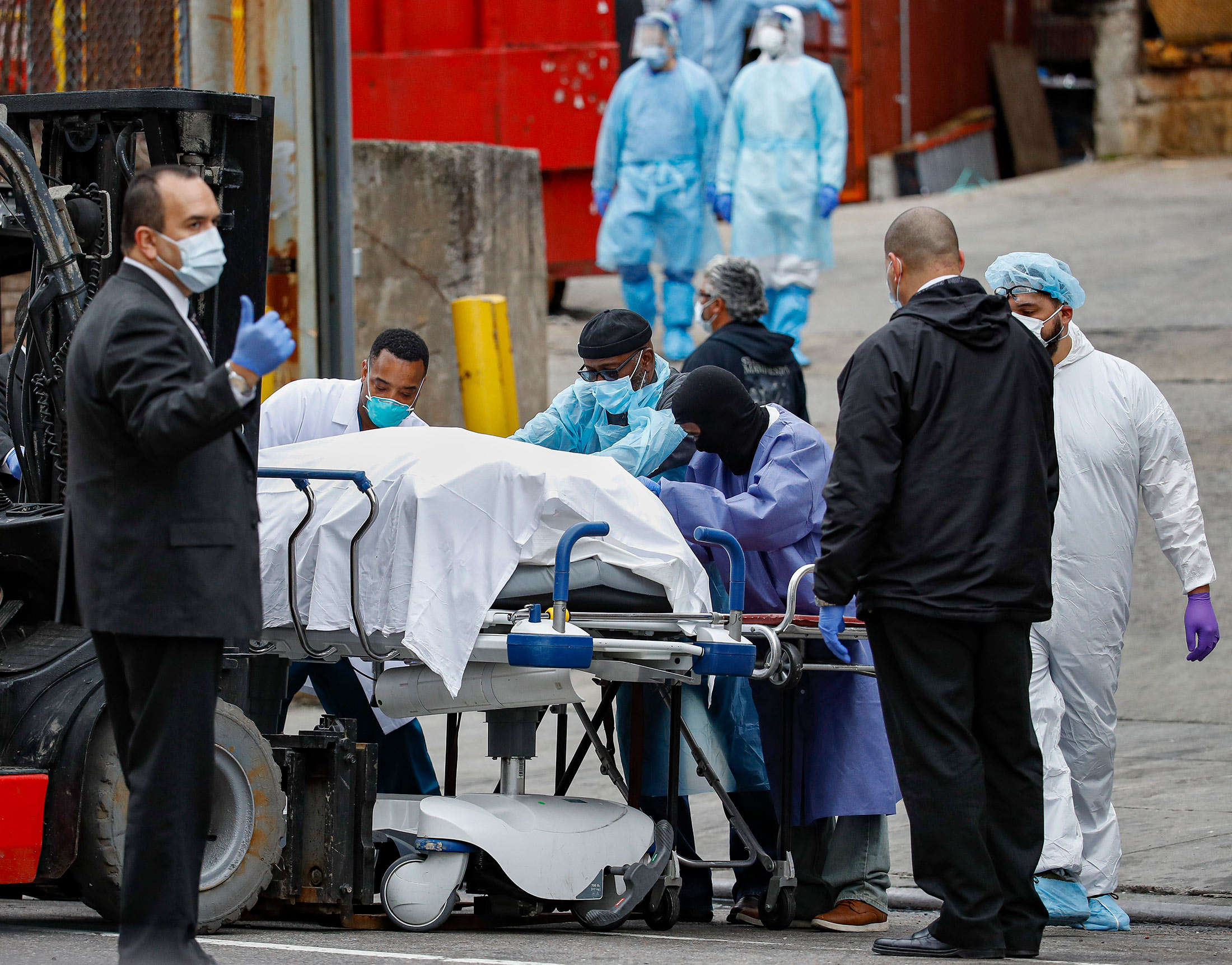 A body wrapped in plastic that was unloaded from a refrigerated truck is handled by medical workers wearing personal protective equipment due to COVID-19 concerns, Tuesday, March 31, 2020, at Brooklyn Hospital Center in Brooklyn borough of New York. The body was moved to a hearse to be removed to a mortuary. The new coronavirus causes mild or moderate symptoms for most people, but for some, especially older adults and people with existing health problems, it can cause more severe illness or death. (AP Photo/John Minchillo)