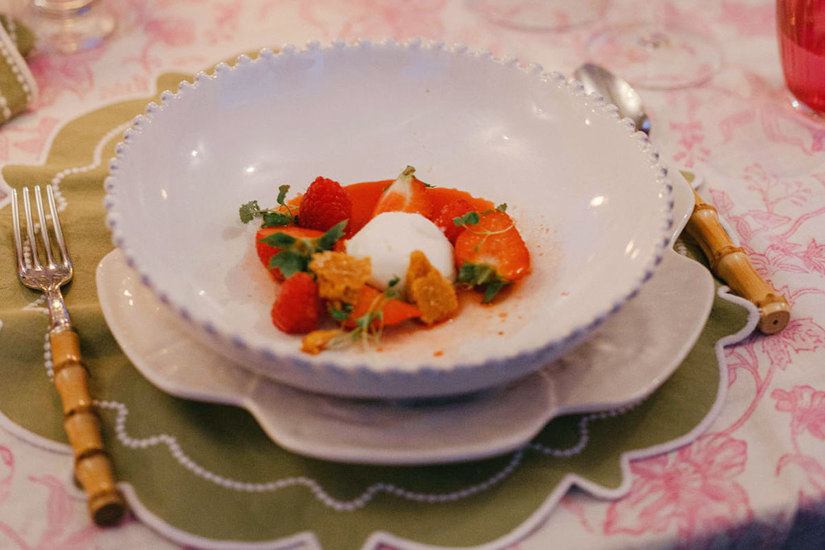 A shallow bowl of sliced strawberries with their tops on, raspberries and cream garnished with sprouts