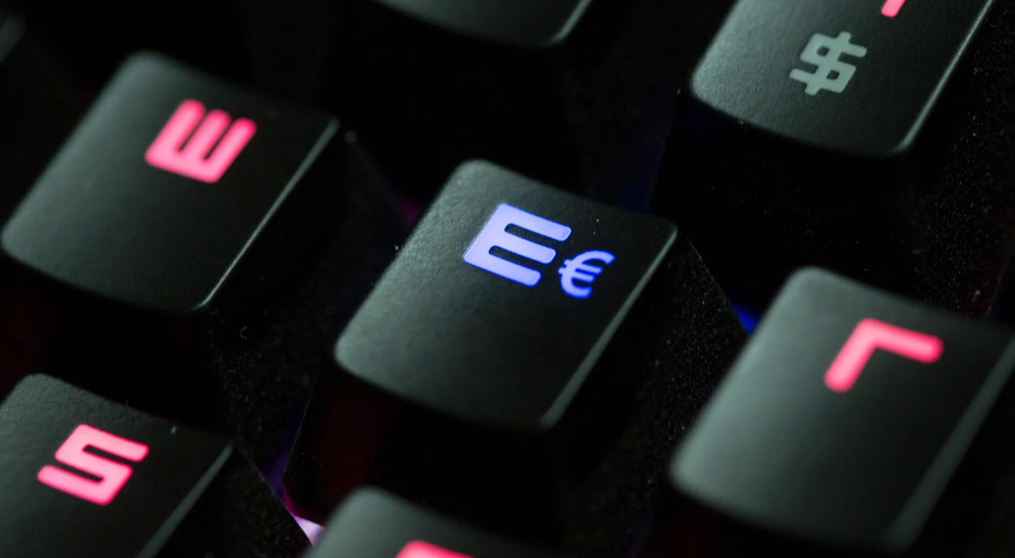 Computer keyboard glows red with blue illuminated euro symbol.
