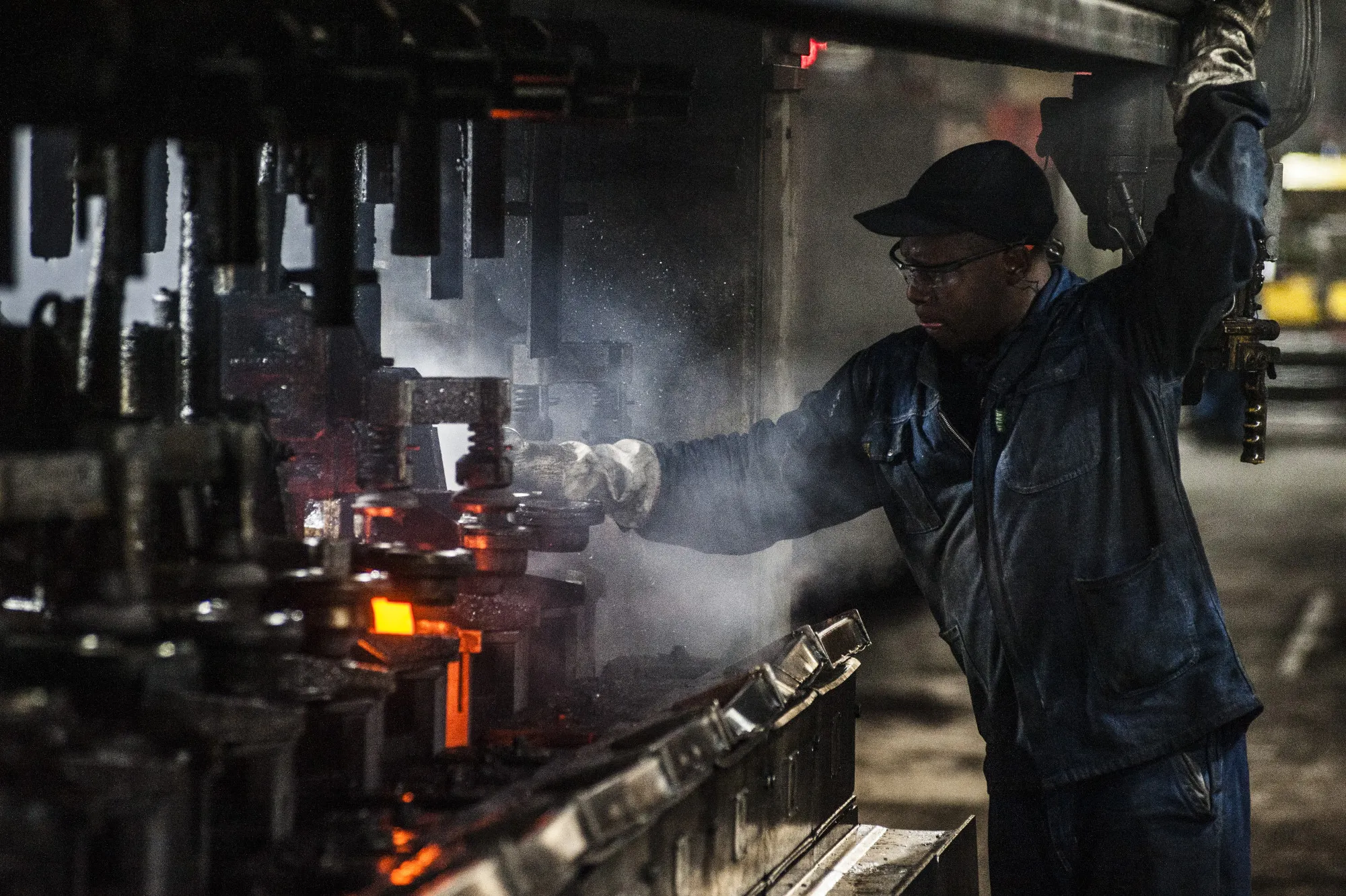 A worker operates a machine used to mold clear glass bottles at a manufacturing plant in Roodekop.
