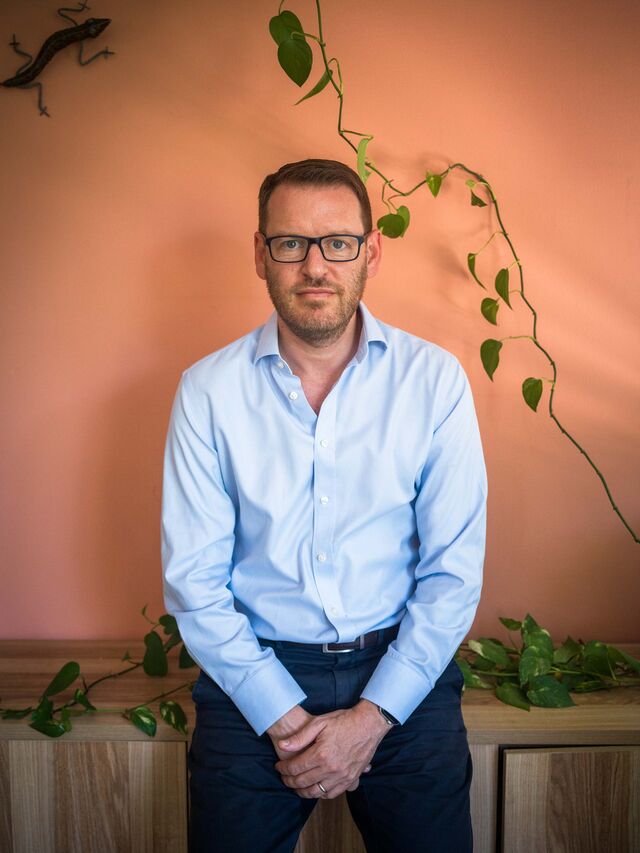 Portrait Dr. Daniel Goldstein standing in front of an orange wall at his home in Raanana.