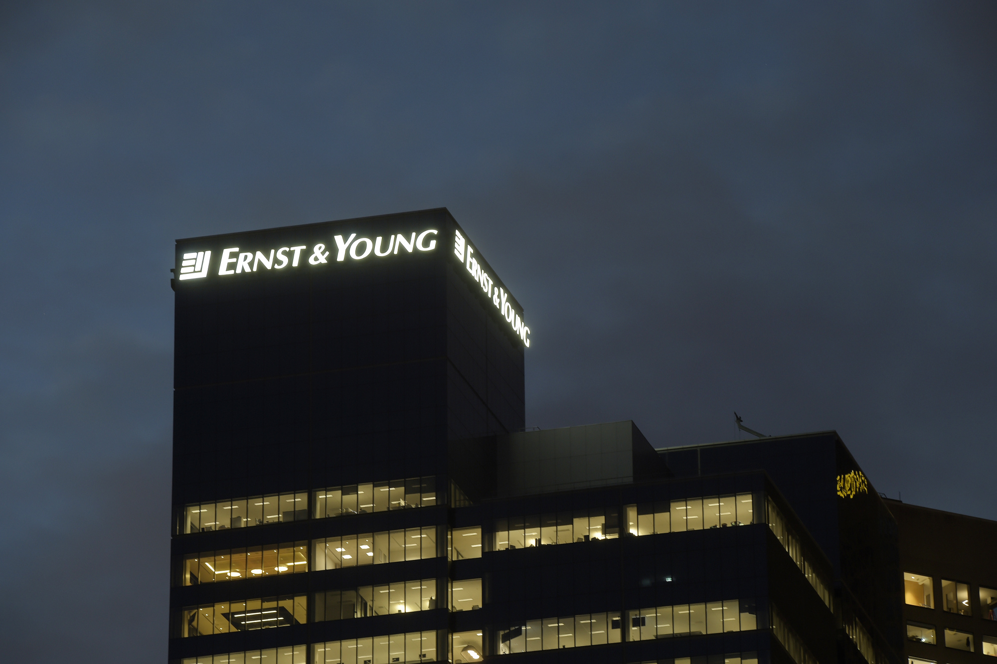 Signage for Ernst &amp; Young LLP is illuminated atop the company's building in Melbourne, Australia.
