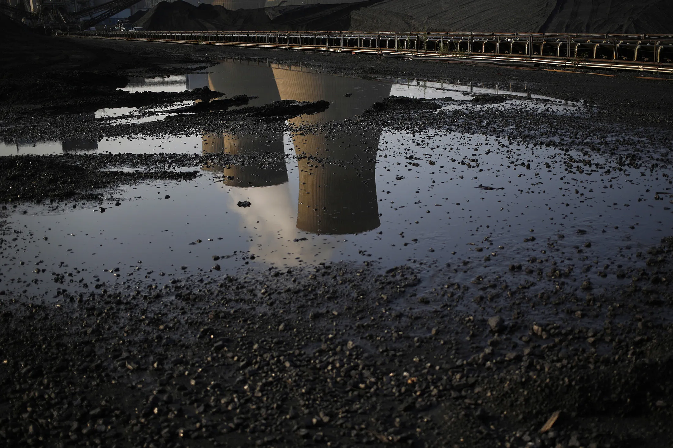 Cooling towers are reflected in a puddle at a coal-fired power plant in Winfield, West Virginia.
