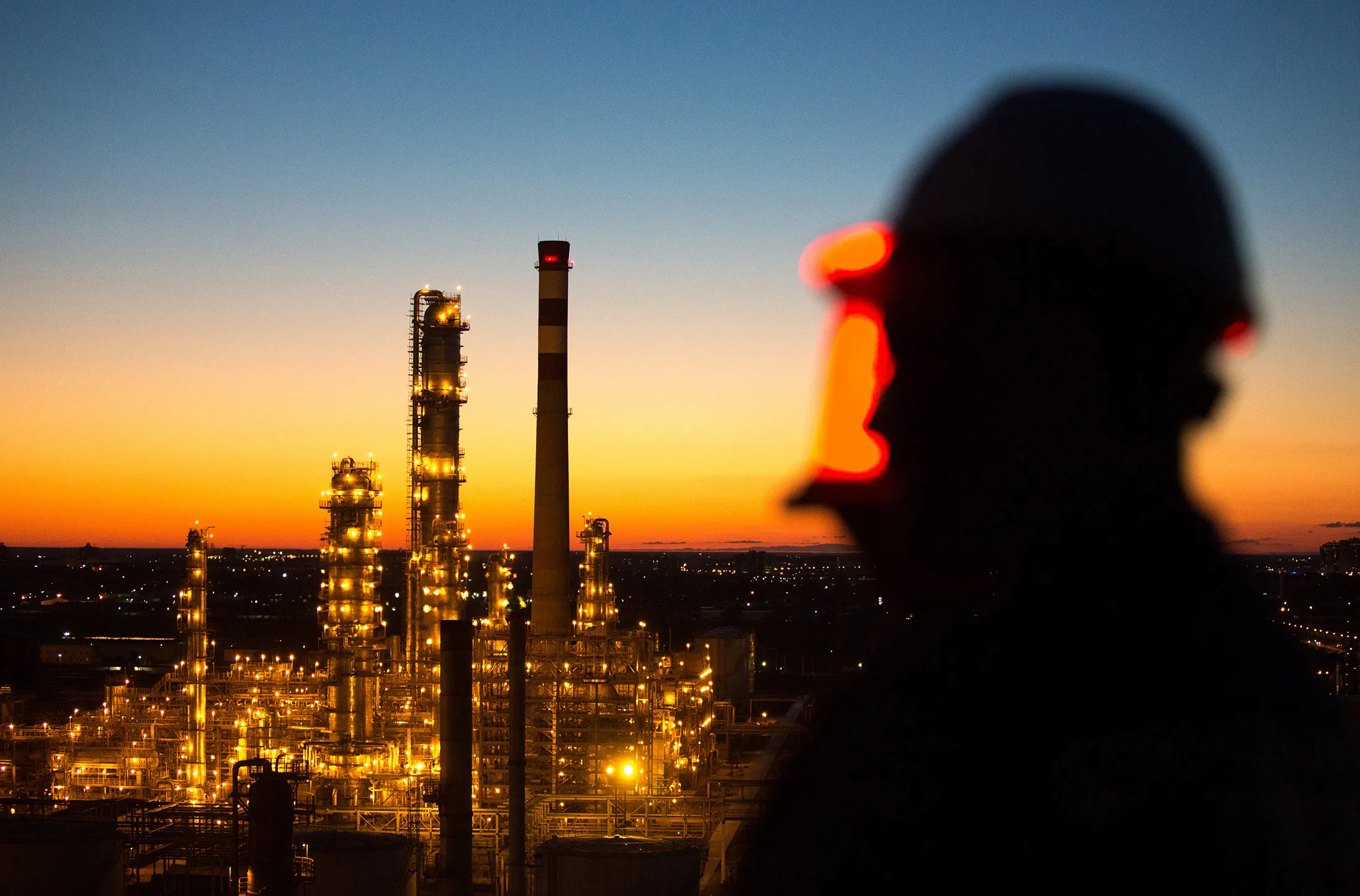 A worker stands on a high level platform and looks out across the illuminated Atyrau oil refinery, operated by KazMunaiGas National Co., in Atyrau, Kazakhstan, on Thursday, July 2, 2015. Kazakhstan is the former Soviet Union's second-largest oil producer.
