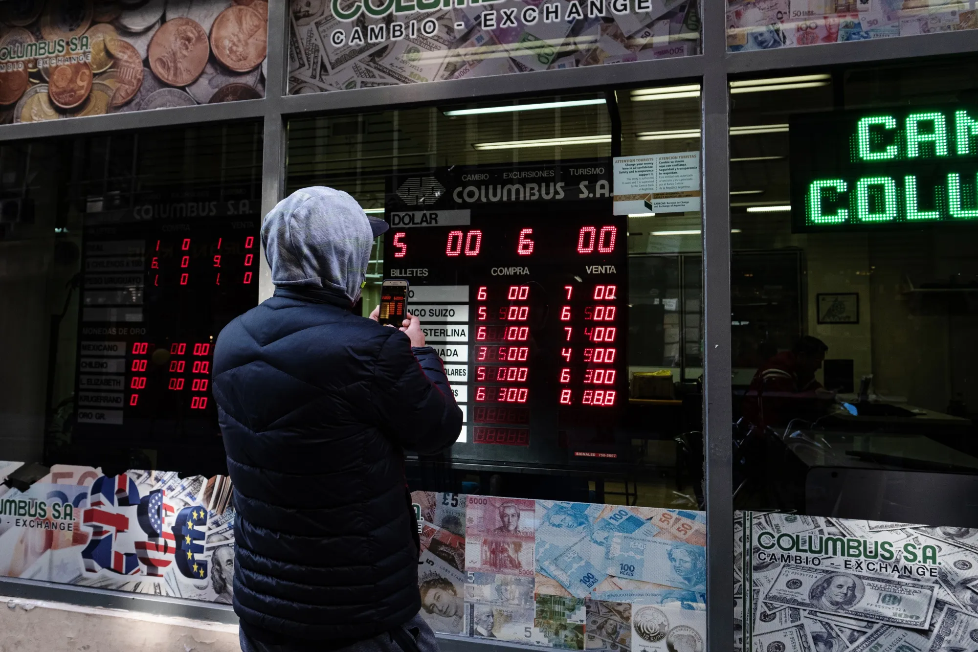 A pedestrian takes a photograph of an electronic monitor displaying the currency exchange rate in Buenos Aires, Argentina.