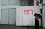A woman holding an umbrella stands next to the logo of Uniqlo at the Ameya Yokocho market in the Ueno district of Tokyo.
