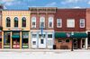 A photo of a typical small town main street in the United States of America. Features old brick buildings with specialty shops and restaurants. Decorated with American flags.