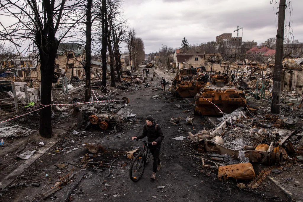 A man pushes his bike through debris and destroyed Russian military vehicles&nbsp;in Bucha, Ukraine in 2022.