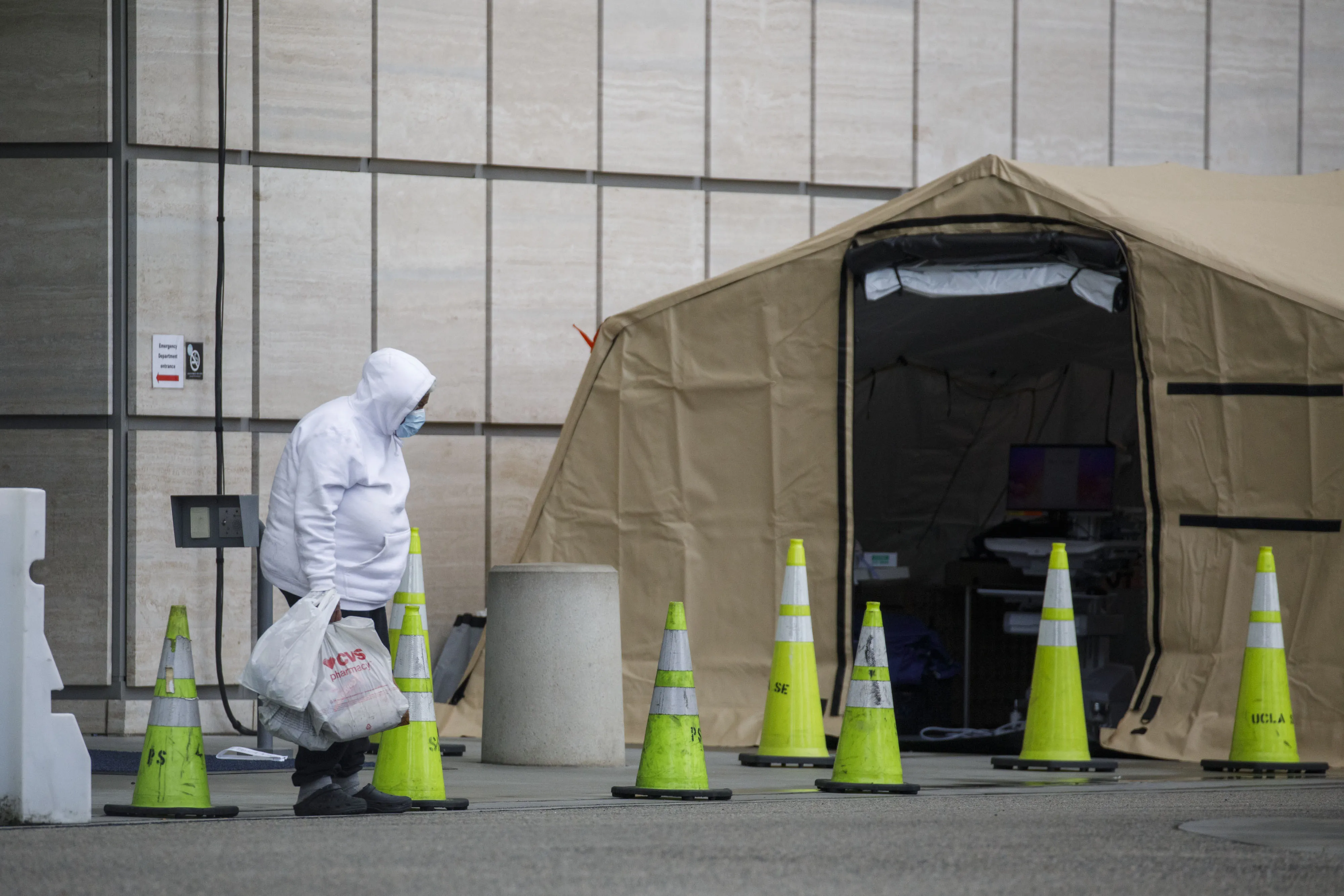 A pedestrian wears a protective face mask while carrying belongings outside of a tent set up for additional capacity and testing outside of the emergency department at Ronald Reagan UCLA Medical Center in Los Angeles, March 19.