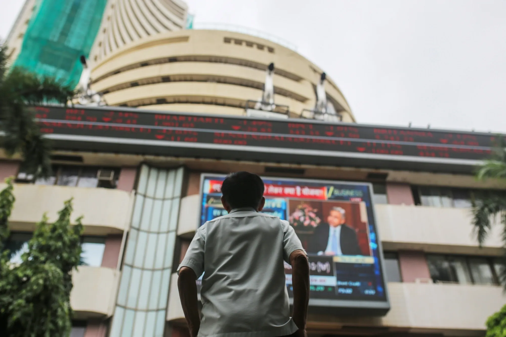 A bystander looks at a screen and a ticker displaying stock prices at the Bombay Stock Exchange (BSE) building in Mumbai.