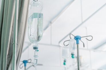 Saline Drip Hanging On Metal Hook Against Wall In Hospital