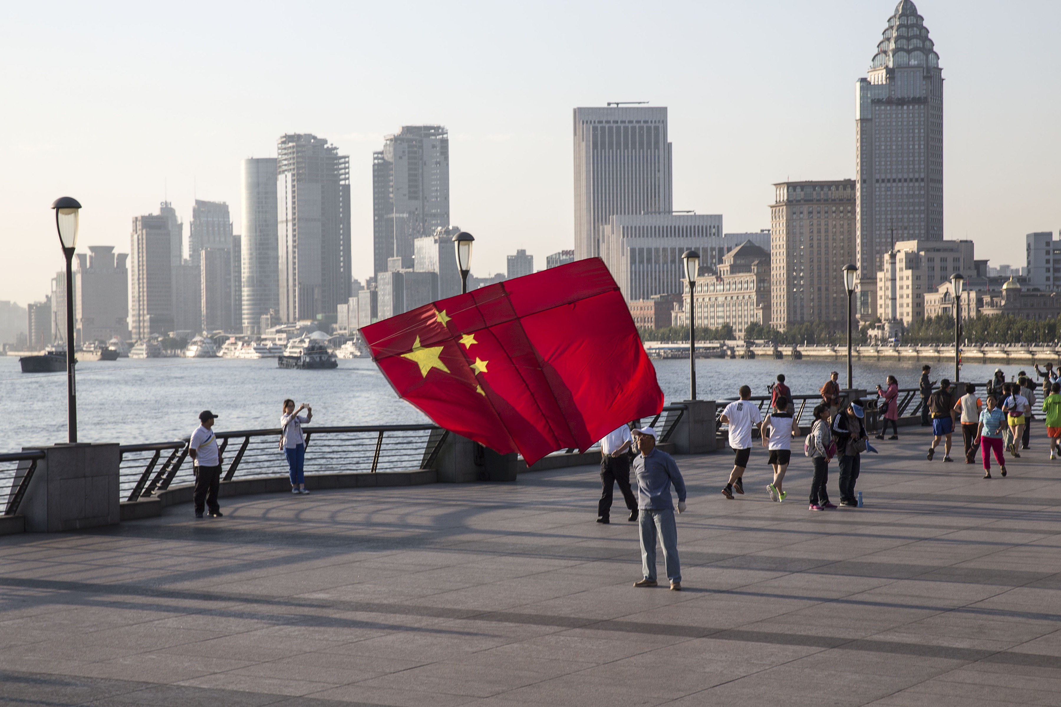 A man launches a kite in the shape of the Chinese national flag on the Bund in Shanghai, China, on Friday, October 2, 2015. China's consumer inflation moderated and deflation at factory doors extended a record high. declines, indicating the People's Bank of China still has room to ease monetary policy further to support a slowing economy.