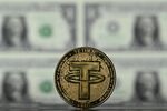 An illustration picture taken in London on May 8, 2022, shows a gold plated souvenir cryptocurrency Tether (USDT) coin arranged beside a screen displaying US dollar notes. Tether (USDT) is an Ethereum token known as a stablecoin that is pegged to the value of the US dollar, and is currently the largest stablecoin with a market value of USD 83 billion dollars. (Photo by Justin TALLIS / AFP) (Photo by JUSTIN TALLIS/AFP via Getty Images)