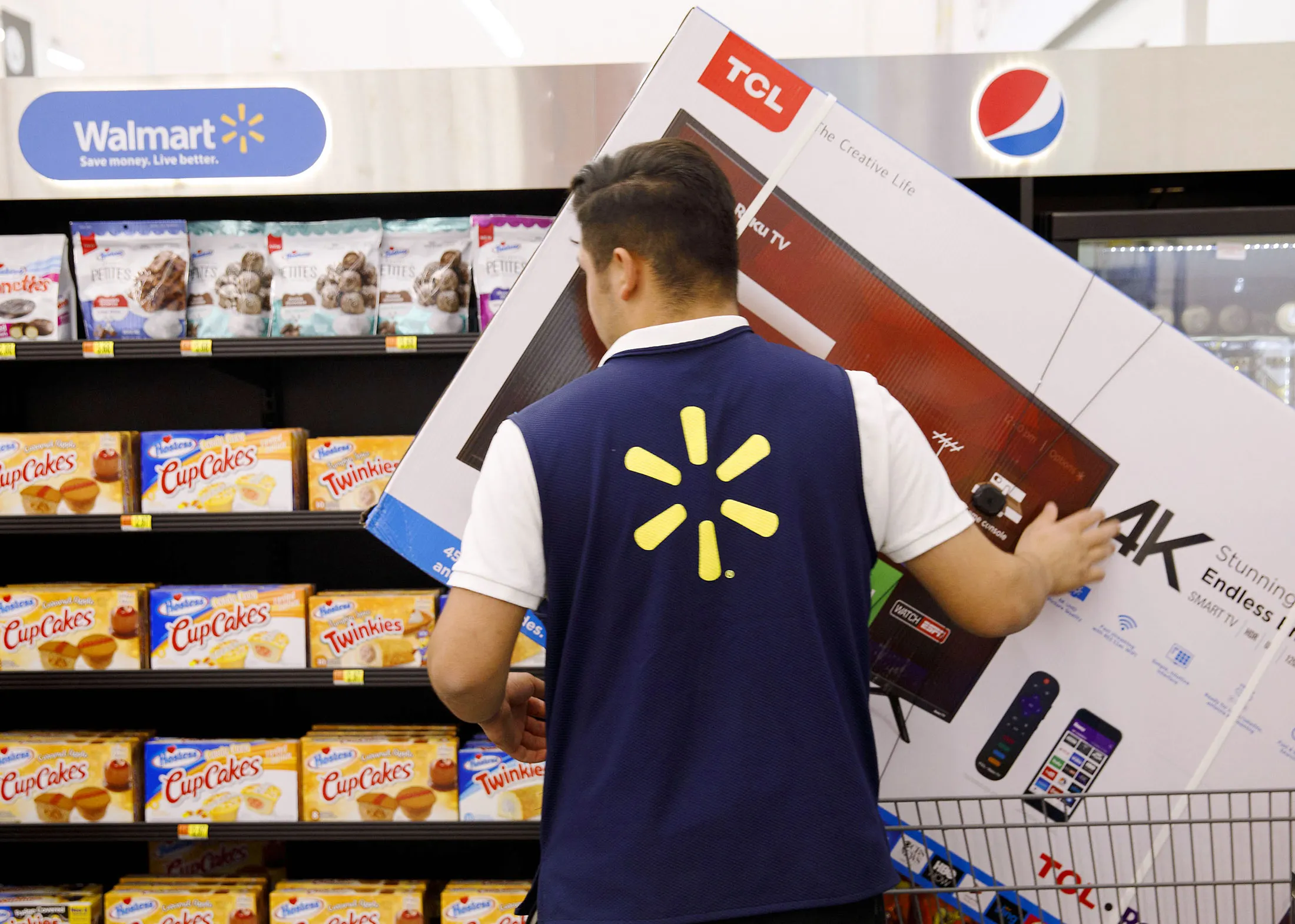 An employee moves a TCL Corp. television in shopping cart at a Walmart&nbsp;location in Burbank, California, U.S.