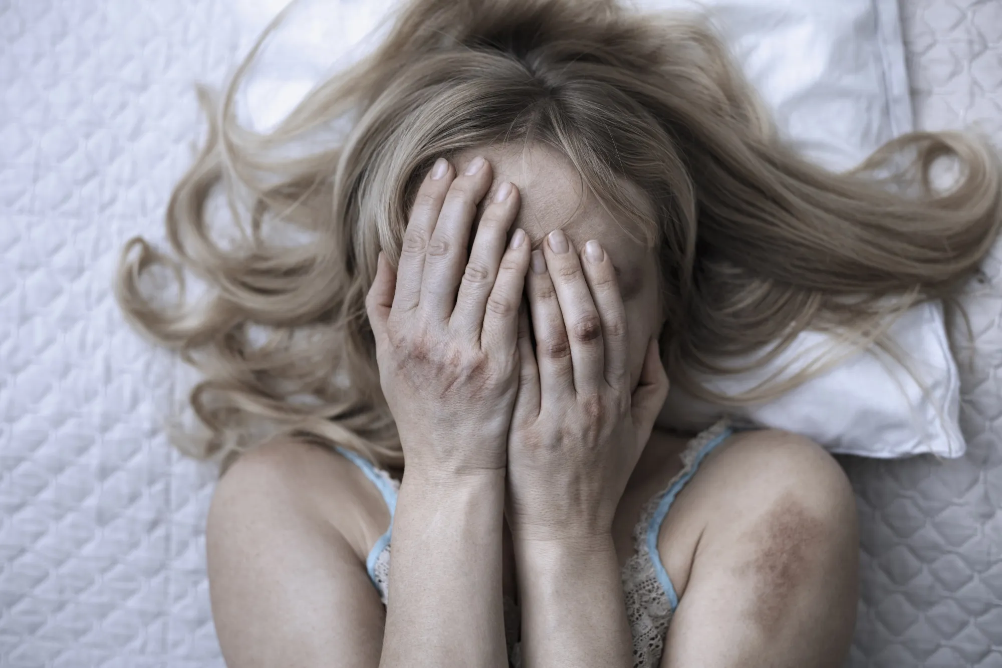 Woman covering face with hands while lying on bed at home