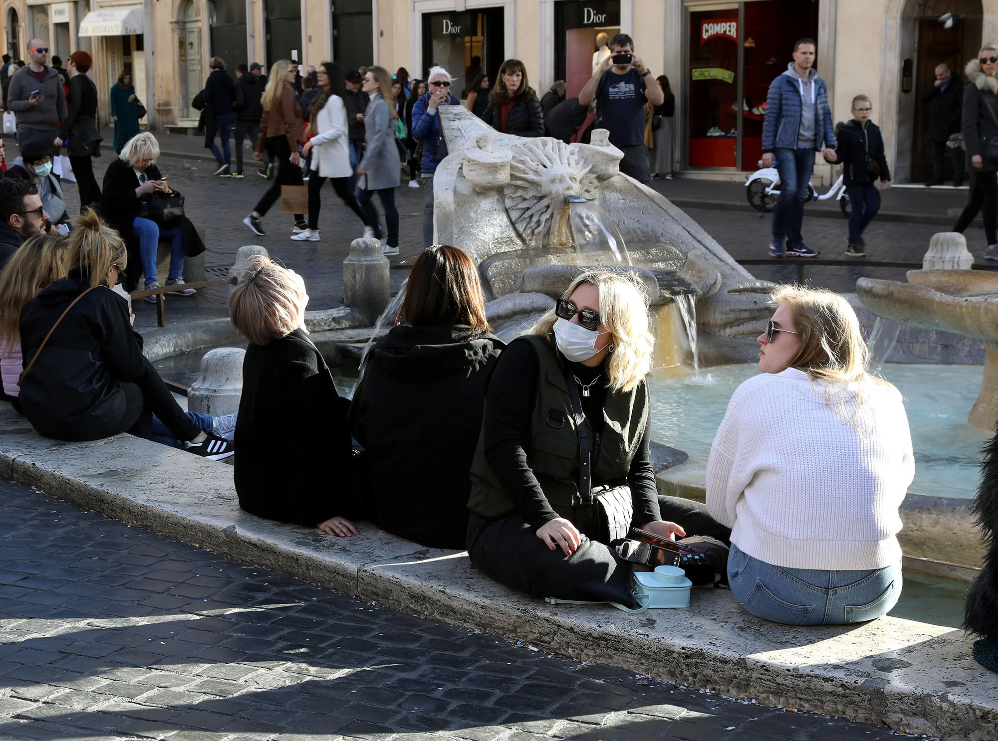 Tourists wearing protective face masks sit at Spain square fountain in Rome on Feb. 25.