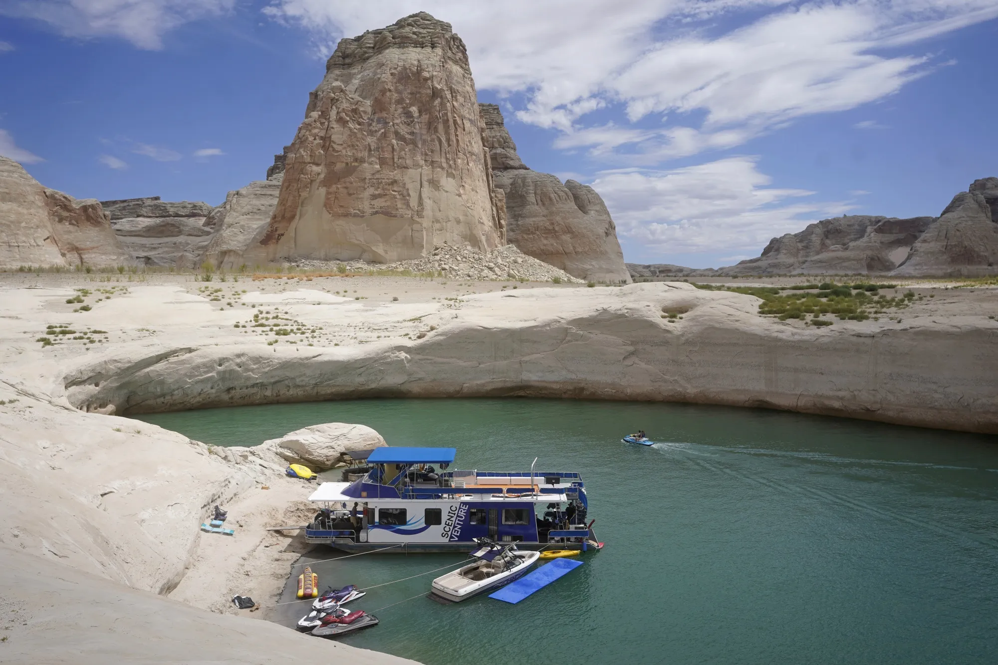 In this Friday, July 30, 2021 file photo, a houseboat rests in a cove at Lake Powell near Page, Ariz. This summer, the water levels hit a historic low amid a climate change-fueled megadrought engulfing the U.S. West.  Severe drought across the West drained reservoirs this year, slashing hydropower production and further stressing the region’s power grids. And as extreme weather becomes more common with climate change, grid operators are adapting to swings in hydropower generation. (AP Photo/Rick Bowmer)