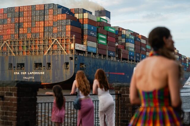 People are seen on the Savannah Riverwalk as a cargo ship passes atter departing the Port of Savannah.