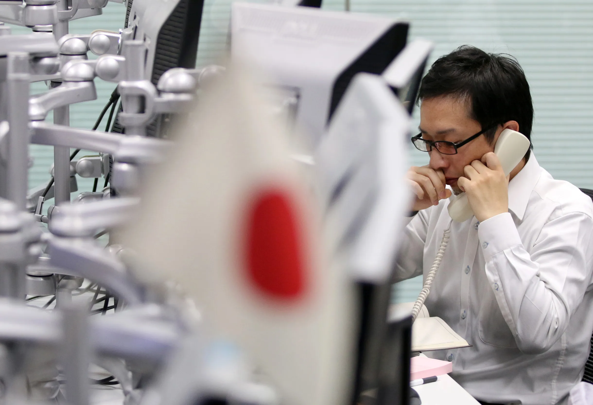 A dealer talks on a phone as a Japanese national flag sits on display.