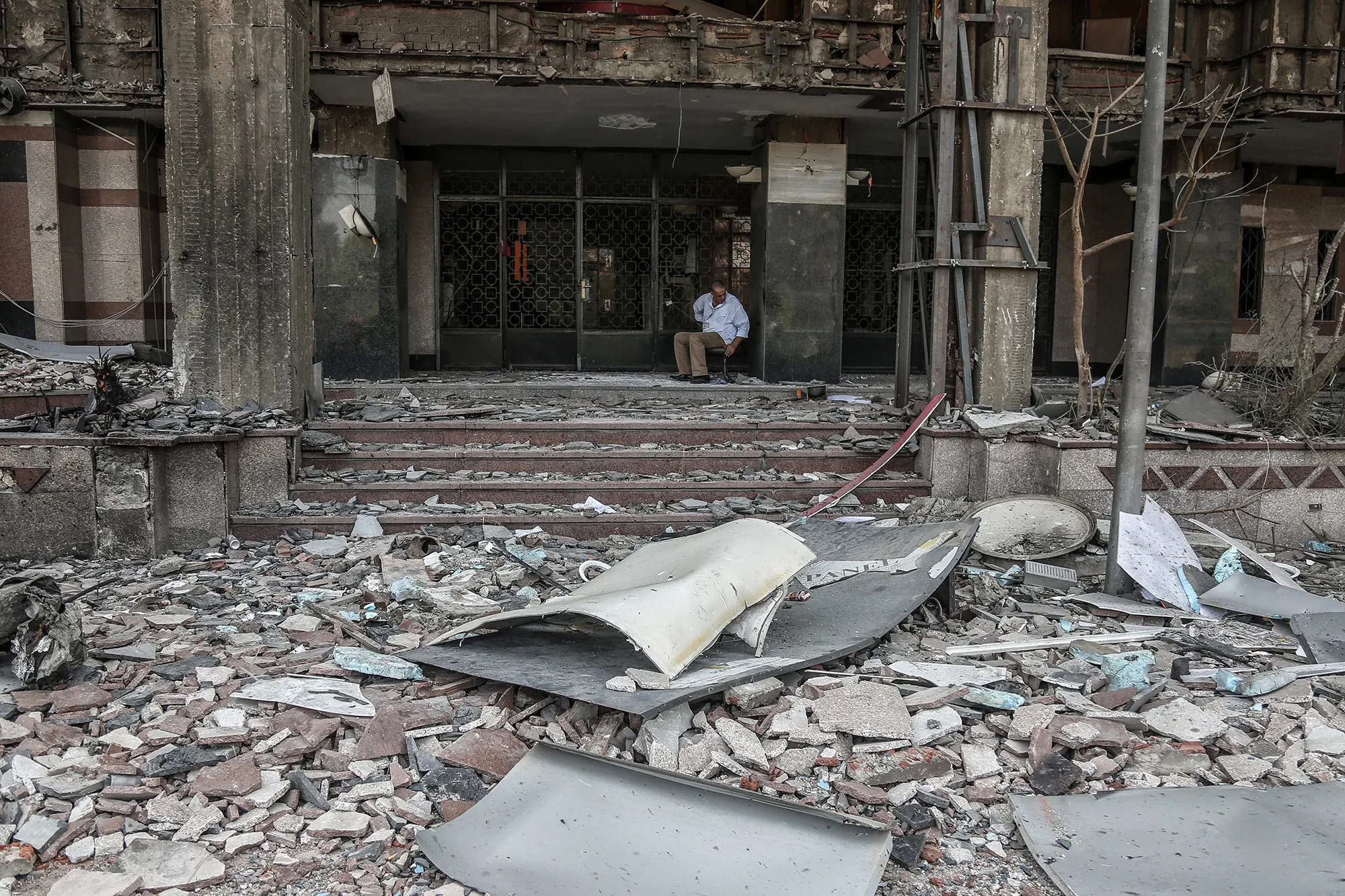 A security guard sits in the damaged facade of the National Cancer Institute after an explosion in Cairo on Aug. 5.