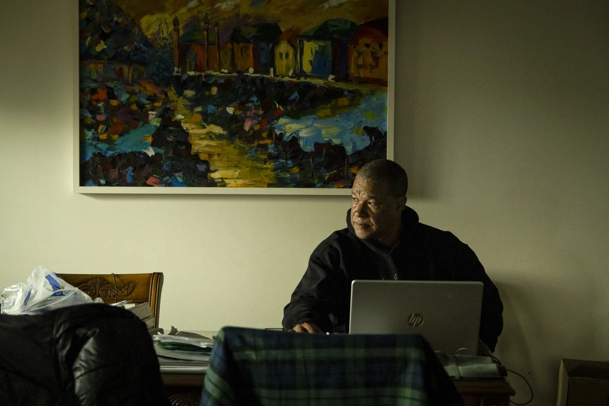 A man sits at his desk,he looks out the window, a laptop is open infront of him.