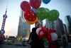 A woman holding balloons walks near Oriental Pearl Radio & TV Tower, left, and other commercial buildings at dusk in the Lujiazui district of Shanghai, China, on Thursday, April 23, 2015. China's gross domestic product expanded 7 percent in the three months through March from a year earlier.