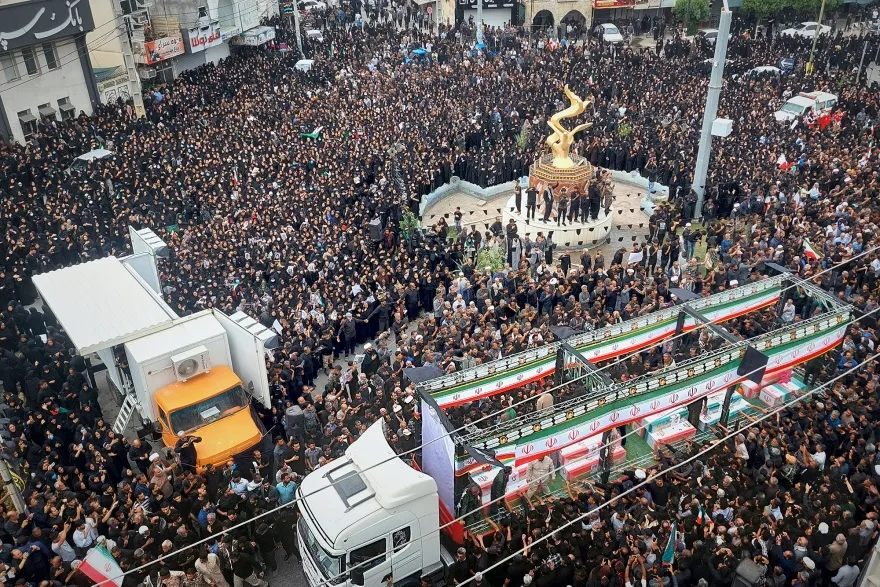 A large square is packed full of people and a truck covered in Iranian flags is surrouded by people.