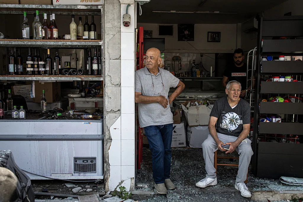 Men sit at the entrance to their damaged shop, following an overnight Iranian missile strike in Bat Yam, Israel