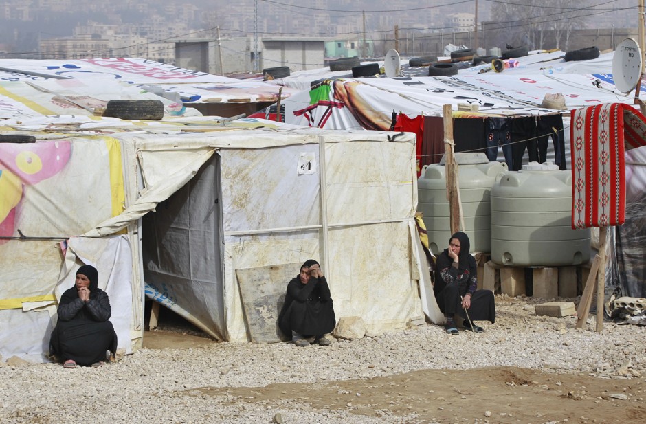 Syrian refugees sit outside their tents at a camp in the Bekaa Valley, Lebanon.