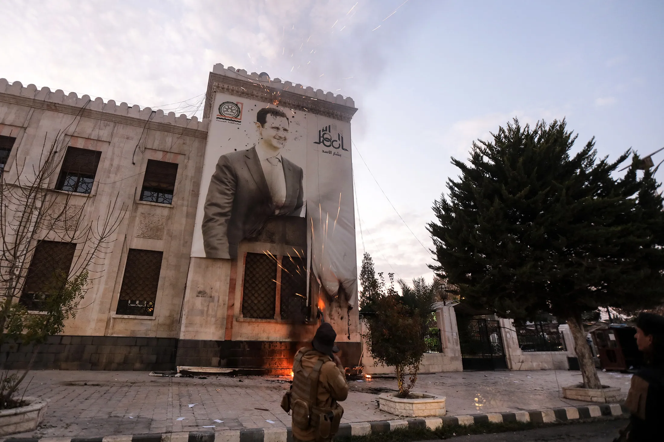 An anti-government fighter shoots against a large banner bearing a picture of Assad, hanging on the facade of a municipal building in Hama on Dec. 5.