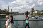 Pedestrians walk over the Quaibruecke, in front of the Grossmuenster church, background right, in Zurich, Switzerland.