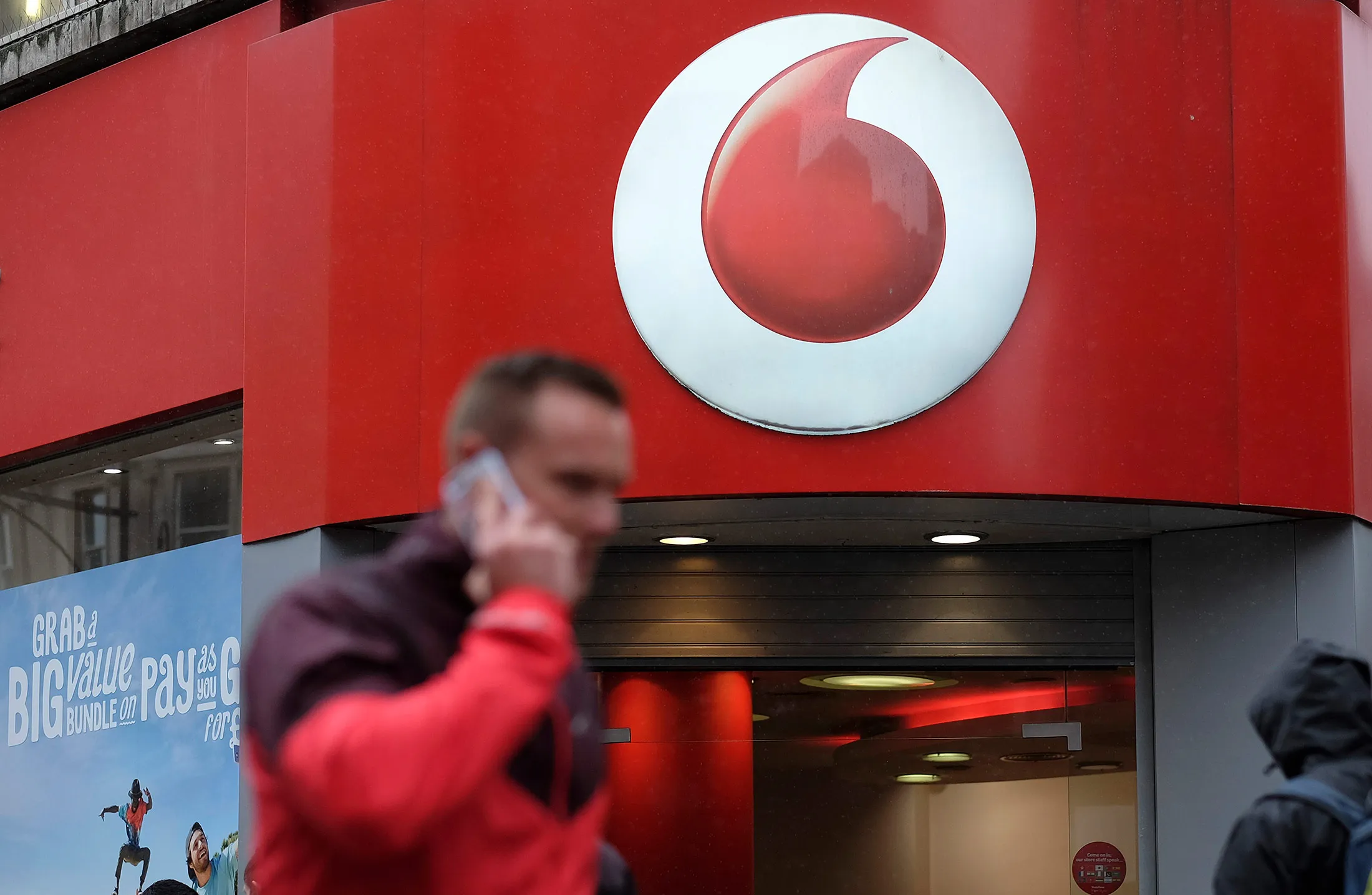 A man talks on a mobile phone outside a Vodafone Group Plc store in London.
