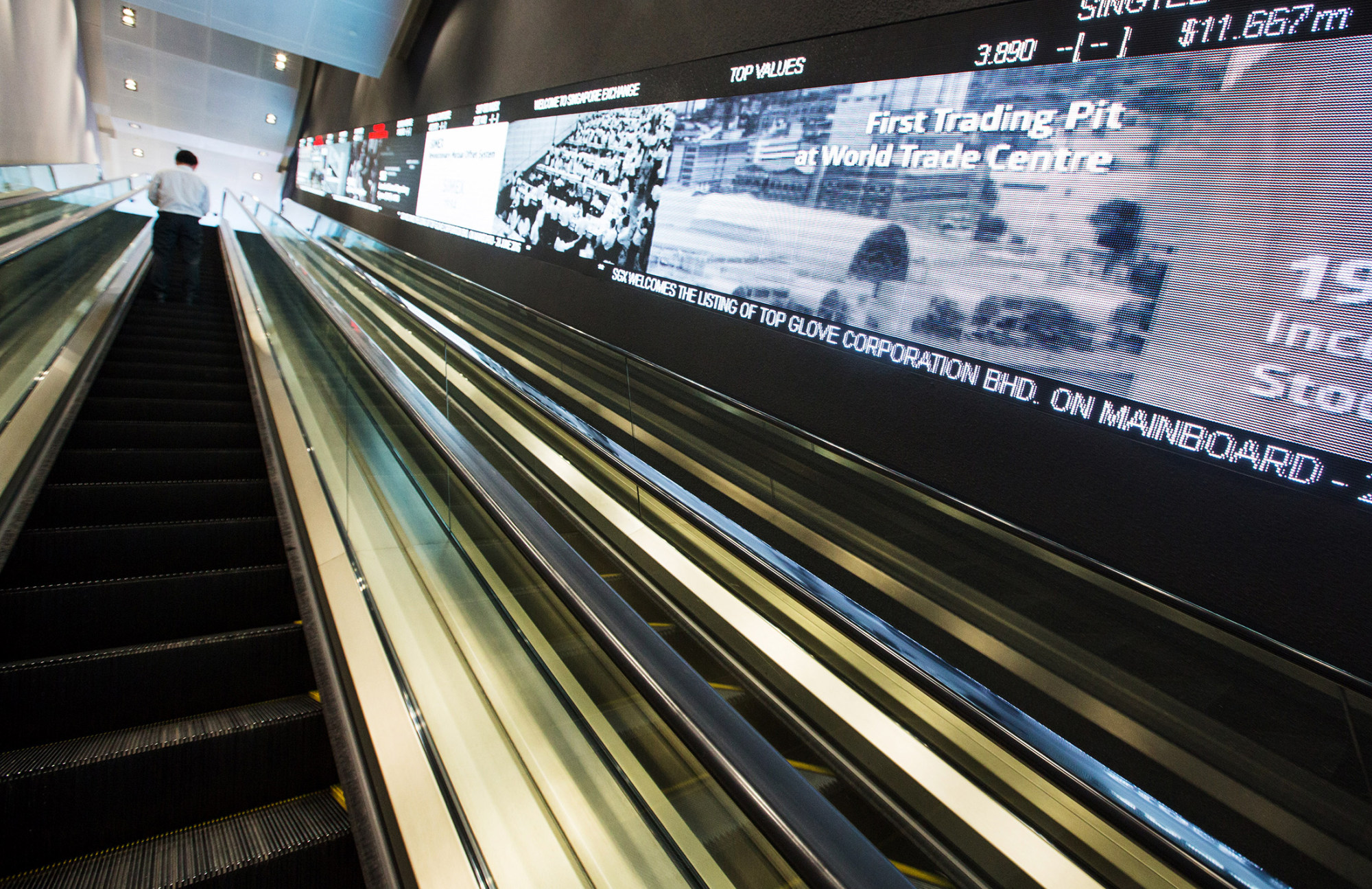 A man rides an escalator past an electronic screen at the Singapore Exchange Ltd.
