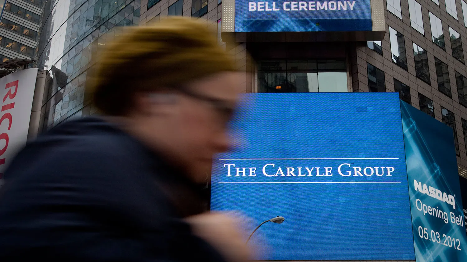 A pedestrian passes in front of the Carlyle Group LP logo displayed on a building in New York on May 3, 2012.
