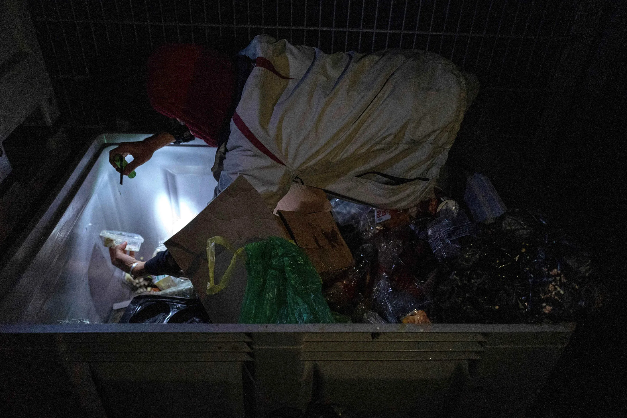 A dumpster diver picks through discarded food items in the back lot of a supermarket in Berlin.
