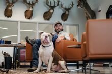 A portriat of Buk Holly sitting in his office with his dog sitting in front of him.