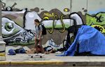 A skateboarder rides past a homeless encampment alongside a street in Los Angeles.