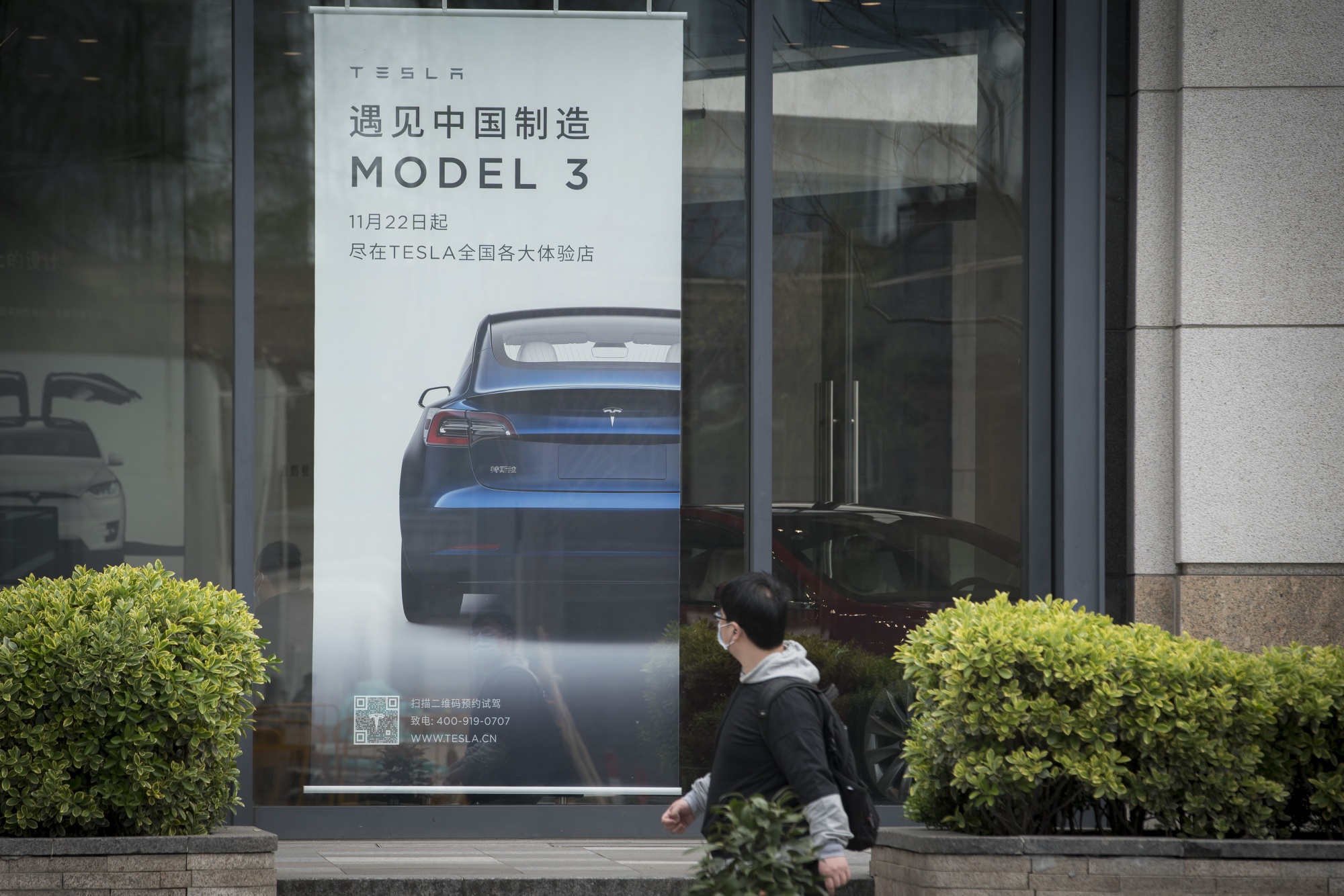 An advertisement for the Tesla Model 3 is displayed at a dealership in Shanghai.
