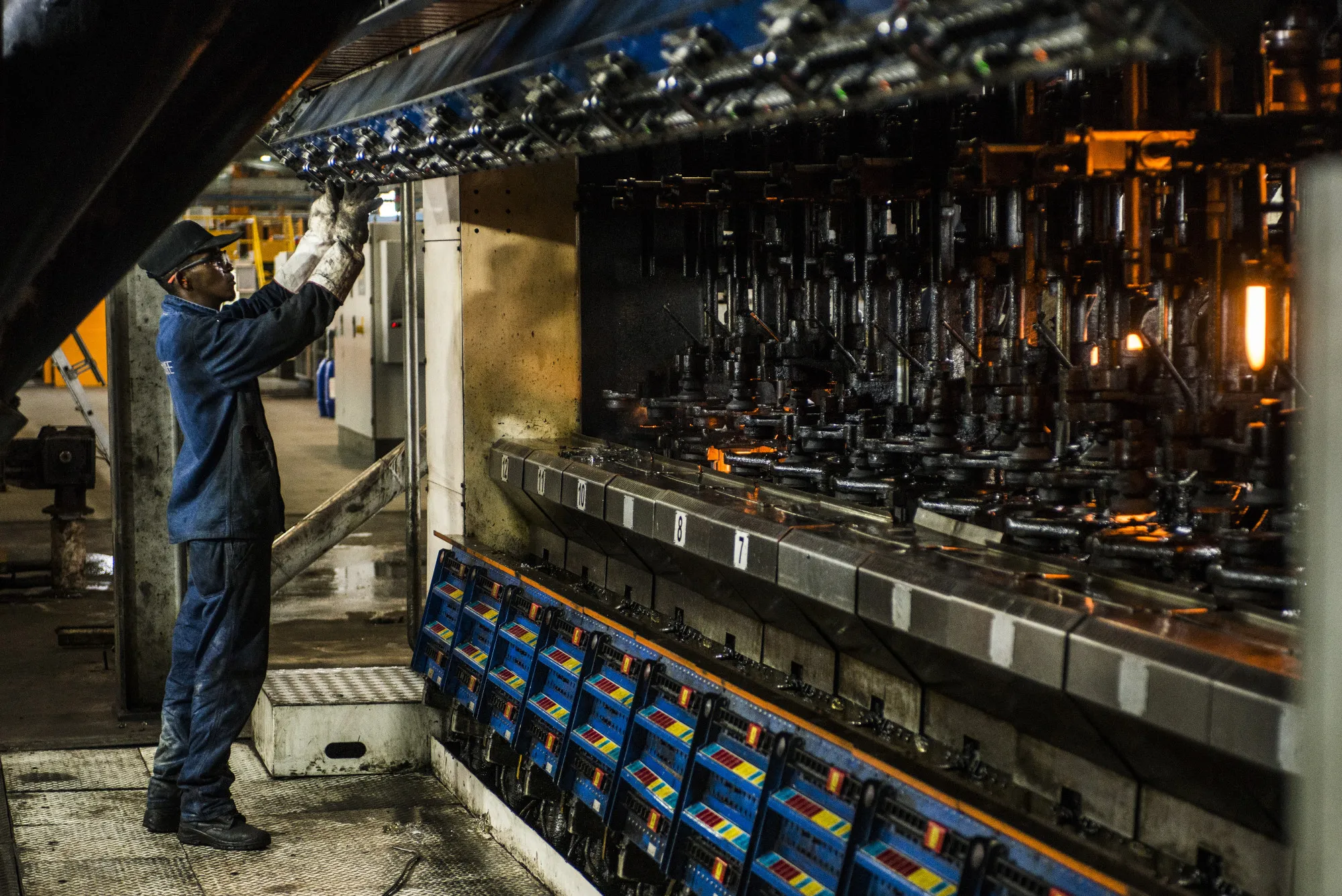 A worker operates a machine used to mold clear glass bottles at a manufacturing plant in Roodekop.