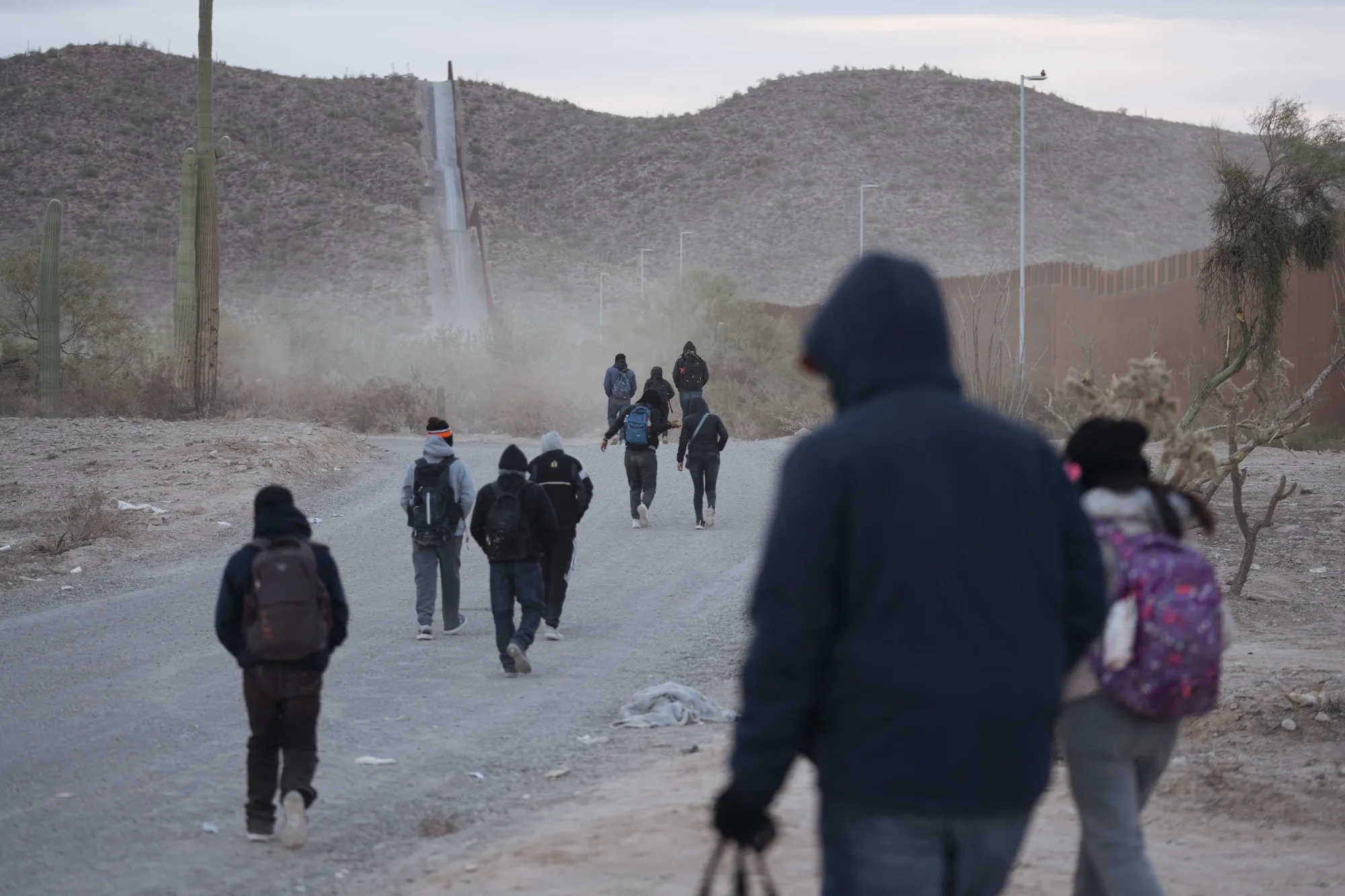 Migrants walk along the border fence at the US-Mexico border in Lukeville, Arizona.