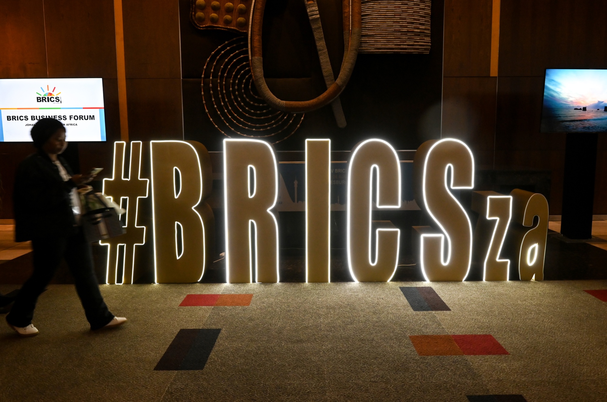 A visitor passes an illuminated sign at&nbsp;the BRICS summit in Johannesburg, South Africa.