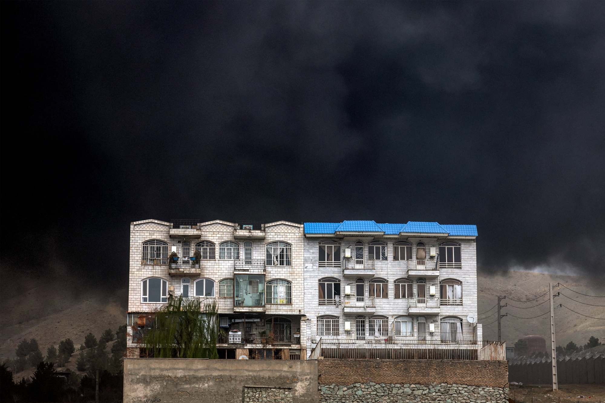 TOPSHOT - A dark smoke cloud engulfs a residential building near an ongoing fire following an overnight airstrike on the Shahran oil refinery in northwestern Tehran on March 8, 2026. The United States and Israel launched strikes against Iran on February 28, sparking swift retaliation by the Islamic republic which responded with missile attacks across the region. The war has dragged in global powers, upended the world's energy and transport sectors, and brought chaos to even usually peaceful areas of the volatile region. (Photo by AFP via Getty Images) Photographer: -/AFP