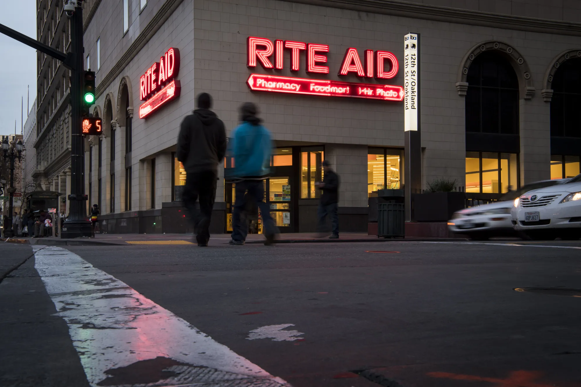 Pedestrians cross a street in front of a Rite Aid Corp. store in Oakland, California.